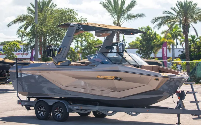 The Image of 2024 Nautique G23 boat on a trailer, parked outdoors with palm trees in the background. - 1