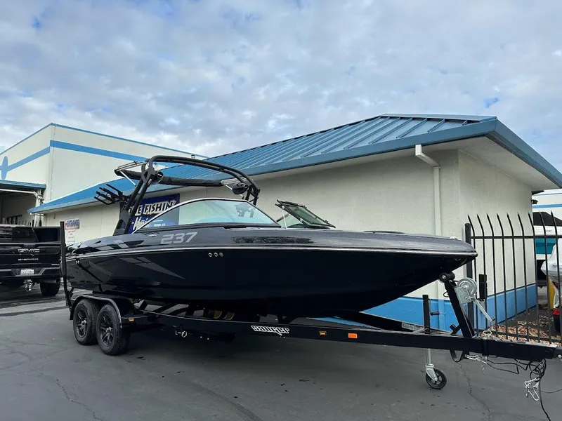 Slide: The Image of 2024 Sanger V237 SX boat on trailer, parked outside building under cloudy sky. - 1