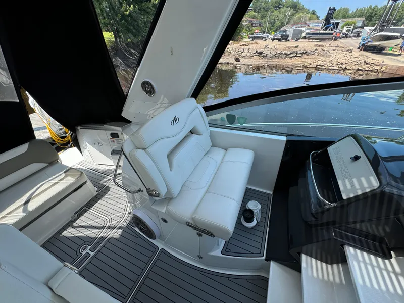 Slide: The Image of 2019 Monterey 335 SY boat interior with white seating and sleek dashboard, docked by a scenic shoreline. - 17