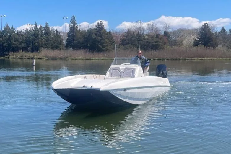 Slide: The Image of 2025 Hustler 25 C3 Speedfish boat cruising on a calm lake with a person at the helm. - 24