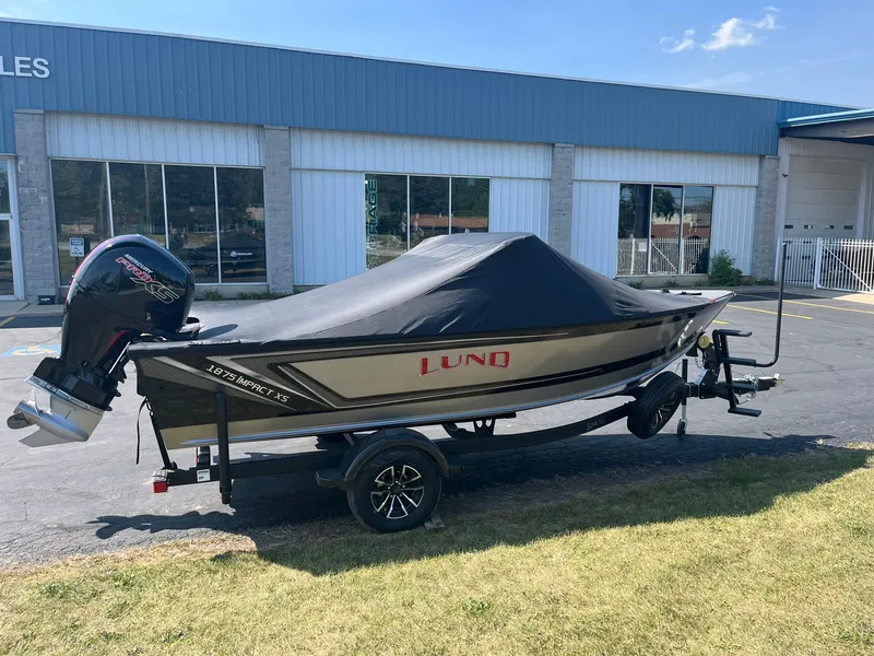 Slide: The Image of 2025 Lund 1875 Impact XS Sport boat with cover on trailer, parked outside dealership. - 29