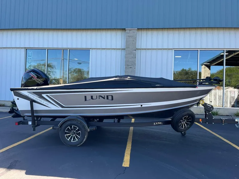 Slide: The Image of 2025 Lund 1775 Impact XS SS boat on trailer, parked outside a building. - 30