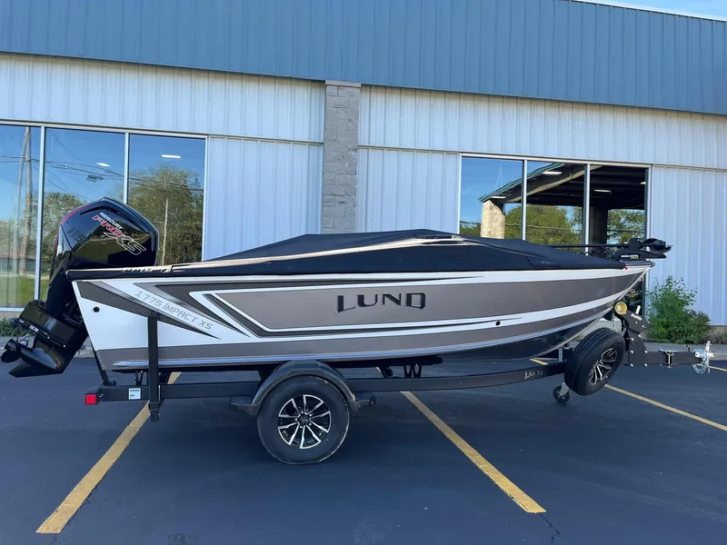 Slide: The Image of 2025 Lund 1775 Impact XS SS boat on trailer, parked outside a building. - 31