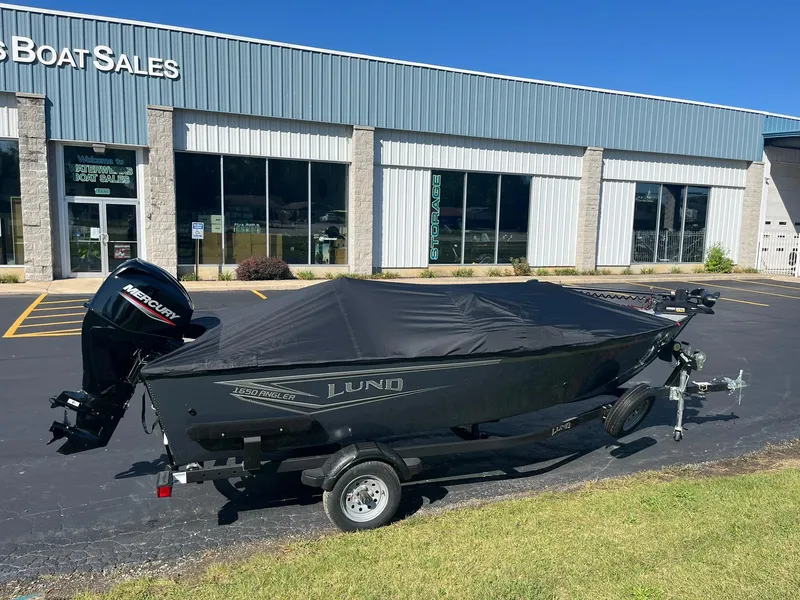 Slide: The Image of 2025 Lund 1650 Angler SS boat with cover, parked outside a sales building. - 24