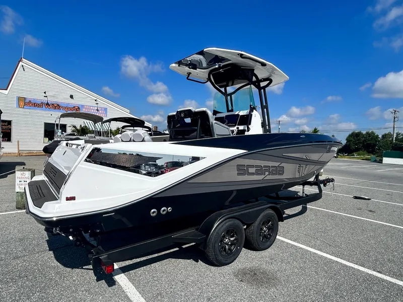 Slide: The Image of 2024 Scarab 255 Open ID boat on trailer in parking lot under clear blue sky. - 7