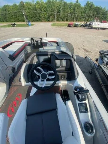 Slide: The Image of 2024 Manitou XT RFXW SHP boat interior with steering wheel and dashboard, parked outdoors. - 6
