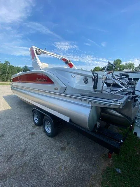 Slide: The Image of 2024 Manitou XT RFXW SHP pontoon boat on trailer, parked outdoors under blue sky. - 7