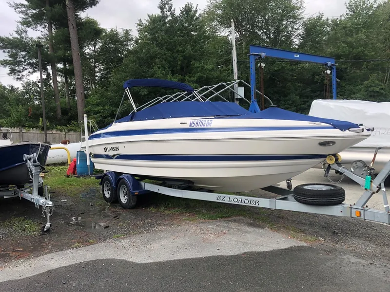 Slide: The Image of 2006 Larson 248 LXI boat on trailer, parked outdoors with trees in the background. - 4