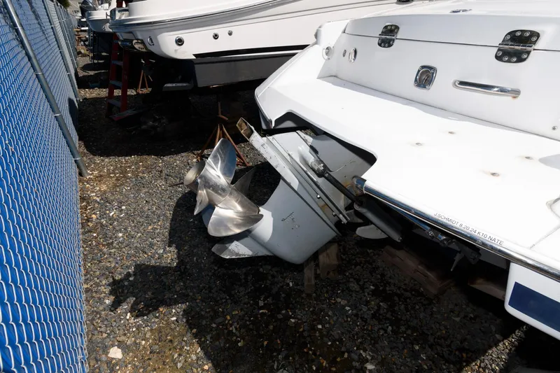 Slide: The Image of 2001 Chris-Craft Launch 22 boat propeller and stern, parked on gravel near a blue fence. - 14