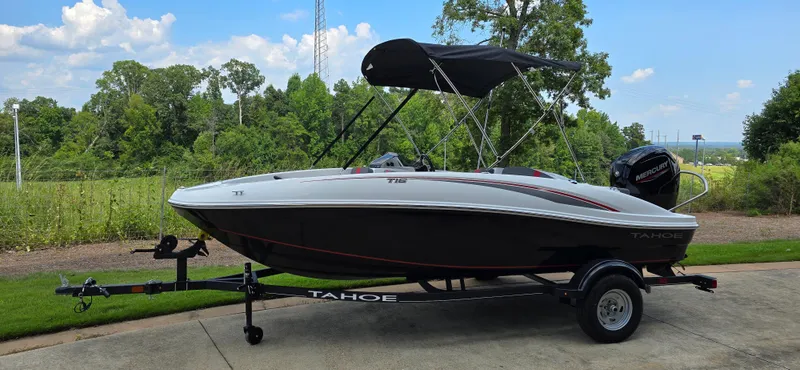 Slide: The Image of 2024 Tahoe T16 boat on trailer, parked outdoors with lush greenery background. - 0