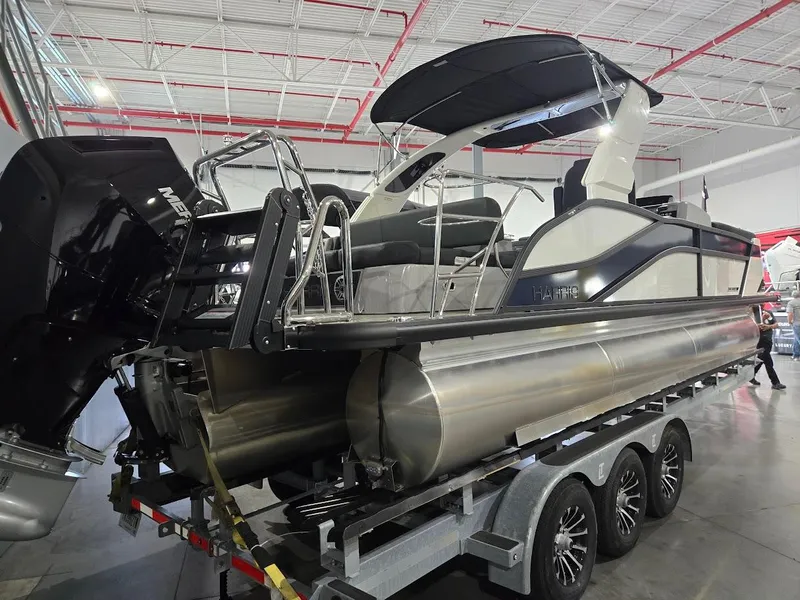 Slide: The Image of 2025 Harris Grand Mariner 250 pontoon boat on a trailer in a showroom. - 2