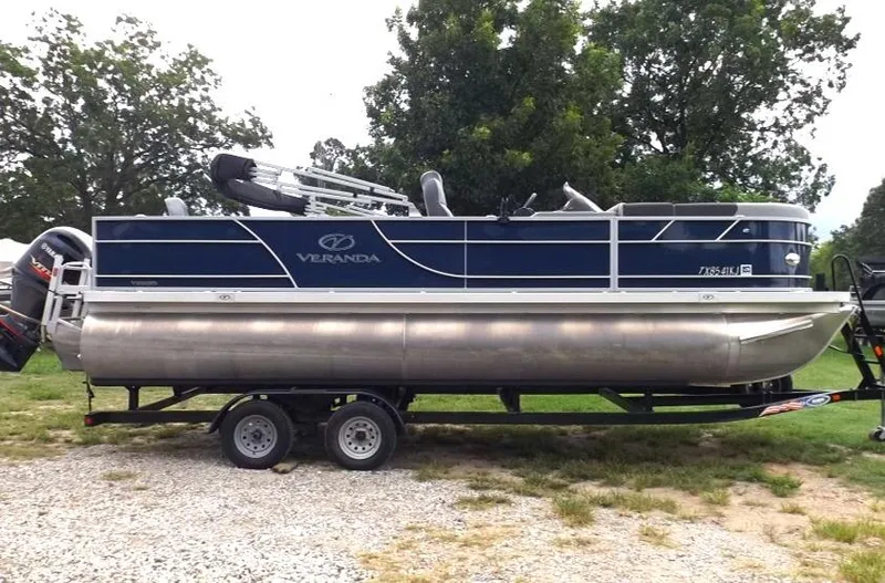 Slide: The Image of 2021 Veranda Fish VF22F2 pontoon boat on a trailer, parked on gravel. - 2