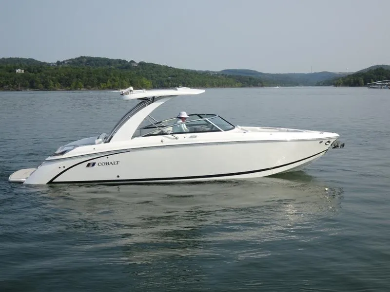 Slide: The Image of 2025 Cobalt R30 boat cruising on a serene lake with lush green hills in the background. - 2