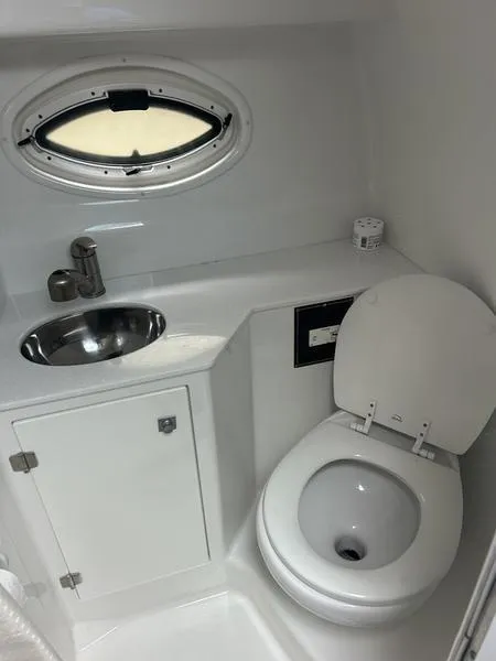 Slide: The Image of 2019 Monterey 295SY boat bathroom with sink, toilet, and porthole window. - 17