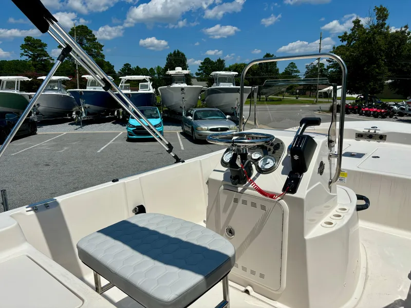 Slide: The Image of 2025 Carolina Skiff 162 JLS boat interior with steering console and seating, parked outdoors. - 4