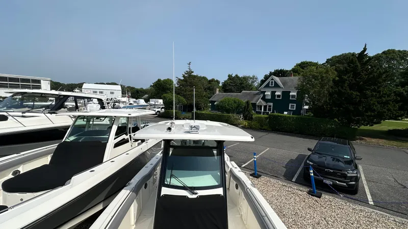 Slide: The Image of 2025 Boston Whaler 330 Outrage boat in a marina with parked cars and greenery. - 35