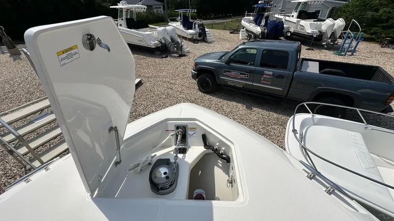 Slide: The Image of 2025 Boston Whaler 330 Outrage anchor compartment, with nearby boats and a truck in the background. - 36
