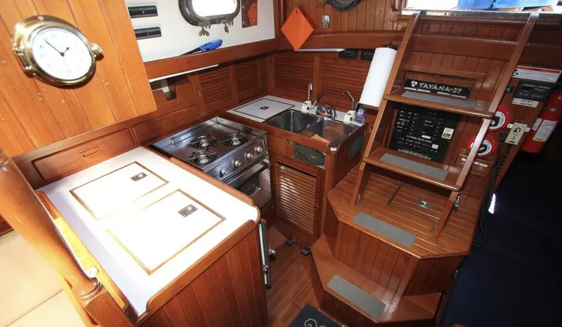 Slide: The Image of 1984 Tayana Sloop Rigged Cutter interior with wooden cabinetry, compact kitchen, and nautical decor. - 13