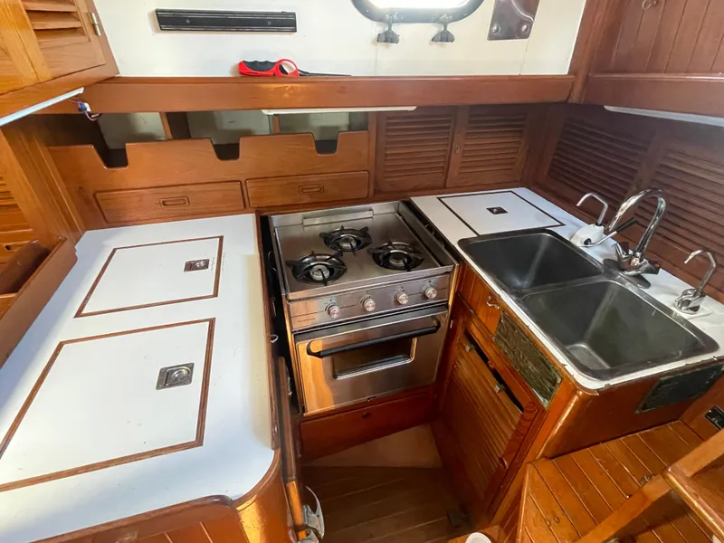 Slide: The Image of 1984 Tayana Sloop Rigged Cutter galley with stove, sink, and wooden cabinetry. - 14