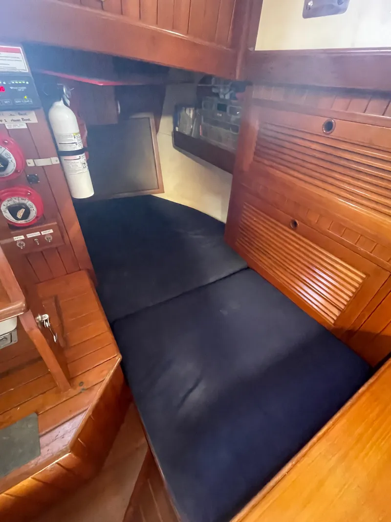 Slide: The Image of 1984 Tayana Sloop Rigged Cutter cabin interior with wooden finish and black cushions. - 26