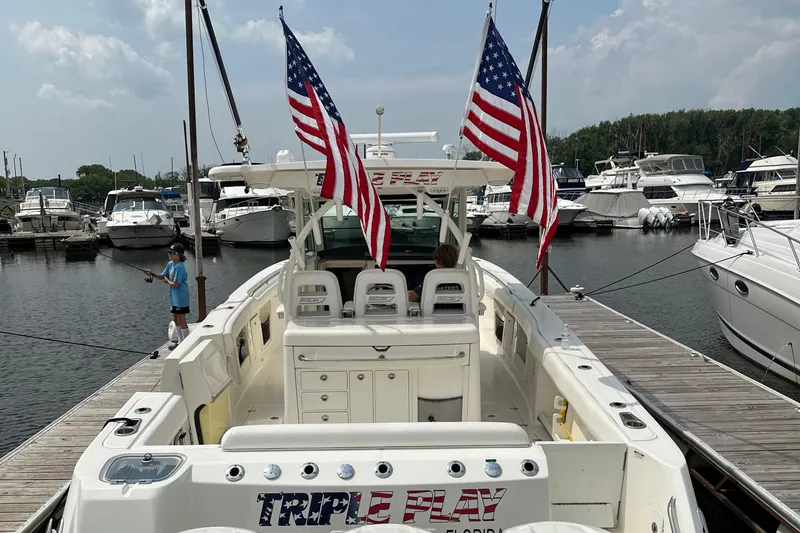 Slide: The Image of 2015 Boston Whaler 370 Outrage docked, displaying American flags, with marina background. - 13
