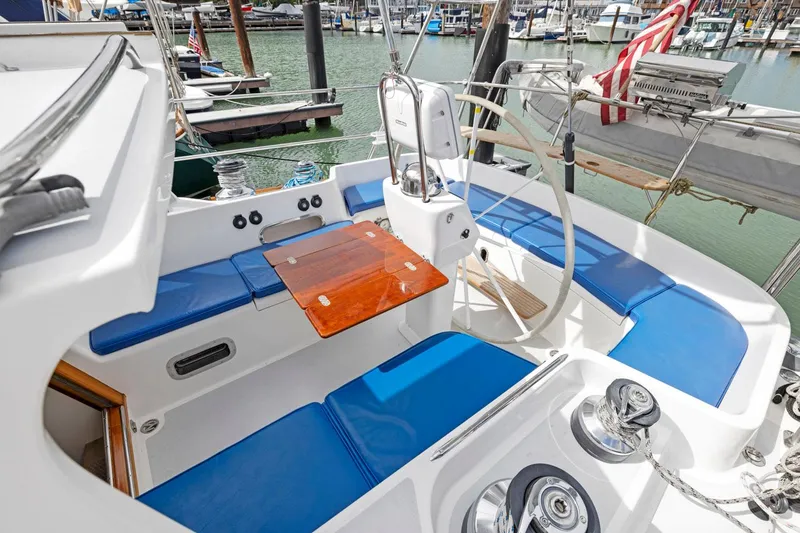 Slide: The Image of Morris 486 sailboat cockpit with blue seating, wooden table, and steering wheel, docked in marina. - 26