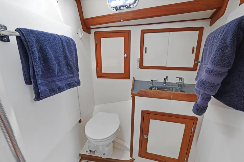 Slide: The Image of Compact boat bathroom with wooden accents, featuring a toilet, sink, and blue towels. Morris 486, 2005. - 44