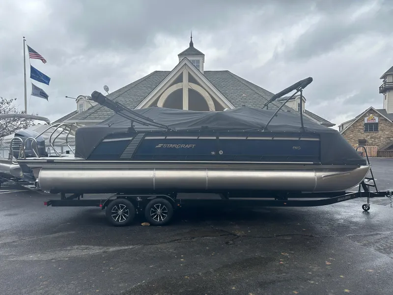 Slide: The Image of 2024 Starcraft MX 25 R pontoon boat on a trailer in front of a building. - 4