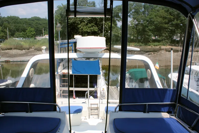 Slide: The Image of 1986 Birchwood 42 Empress yacht docked, featuring blue seating and canopy, surrounded by trees. - 16