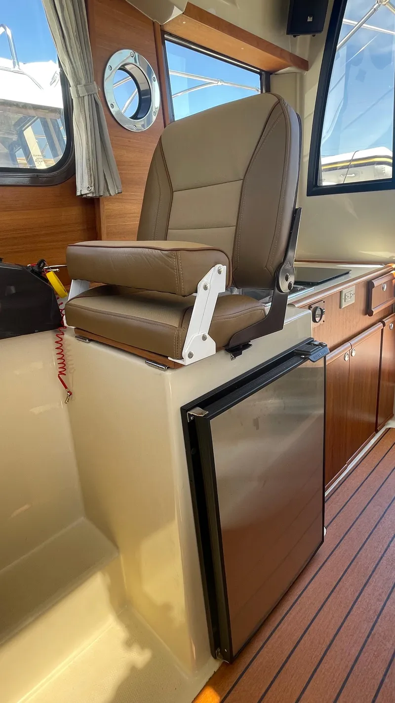Slide: The Image of 2024 Ranger Tugs R-25 interior with captain's chair and compact refrigerator. - 25
