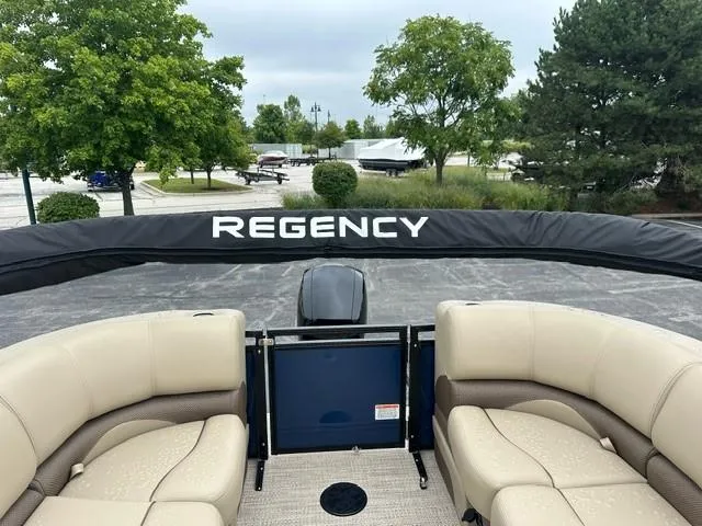 Slide: The Image of 2024 Regency 230 DL3 pontoon boat with beige seating and outdoor backdrop. - 5
