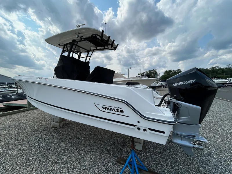 Slide: The Image of 2024 Boston Whaler 230 Outrage boat displayed outdoors with modern buildings in the background. - 3