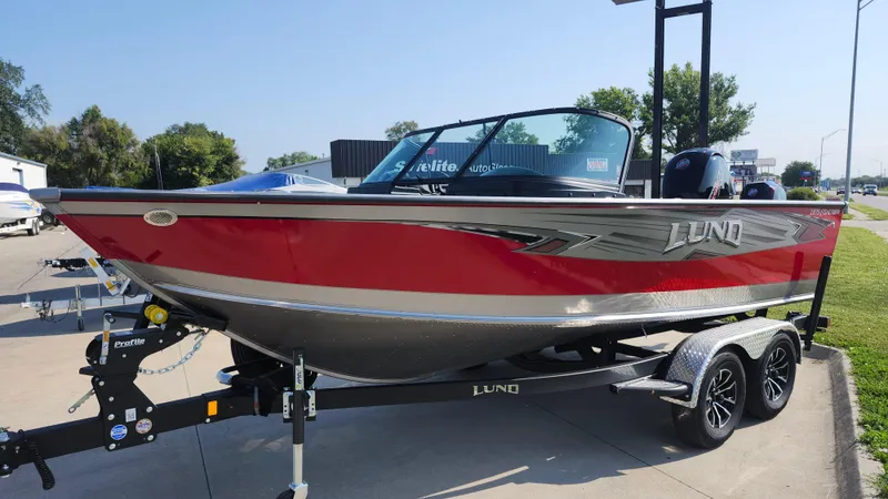 Slide: The Image of 2025 Lund 1875 Fisherman boat, red and silver, on a trailer in a parking lot. - 2
