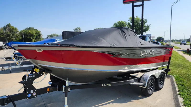 Slide: The Image of 2025 Lund 1875 Fisherman boat, red and black, covered, on a trailer in a parking lot. - 9