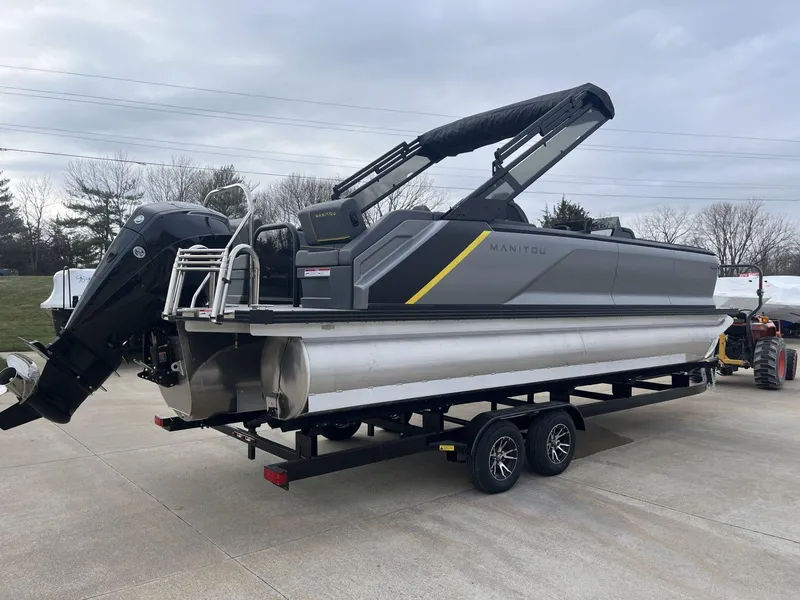 Slide: The Image of 2024 Manitou Explore 24 Navigator pontoon boat on trailer, gray with black and yellow accents. - 2