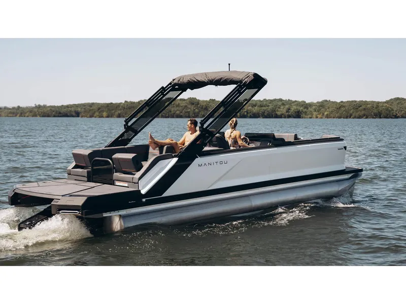 Slide: The Image of 2024 Manitou Explore 24 Navigator pontoon boat cruising on a serene lake. - 24