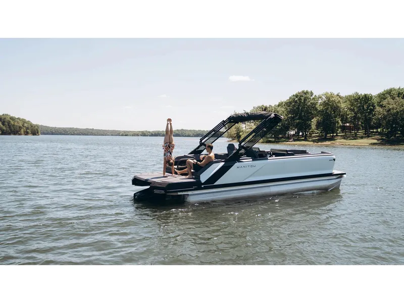 Slide: The Image of 2024 Manitou Explore 24 Navigator pontoon boat on a serene lake. - 25