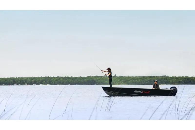 Slide: The Image of 2024 Alumacraft V-16 Tiller boat on a serene lake, two people fishing. - 21
