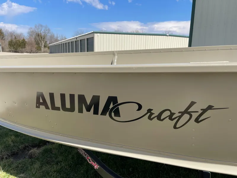 Slide: The Image of 2024 Alumacraft V-16 Tiller boat, beige exterior, parked outdoors near storage building. - 8