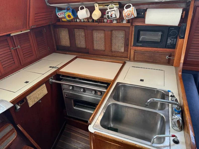 Slide: The Image of 1979 Islander IP Peterson 40 yacht kitchen with stove, sink, microwave, and hanging mugs. - 18