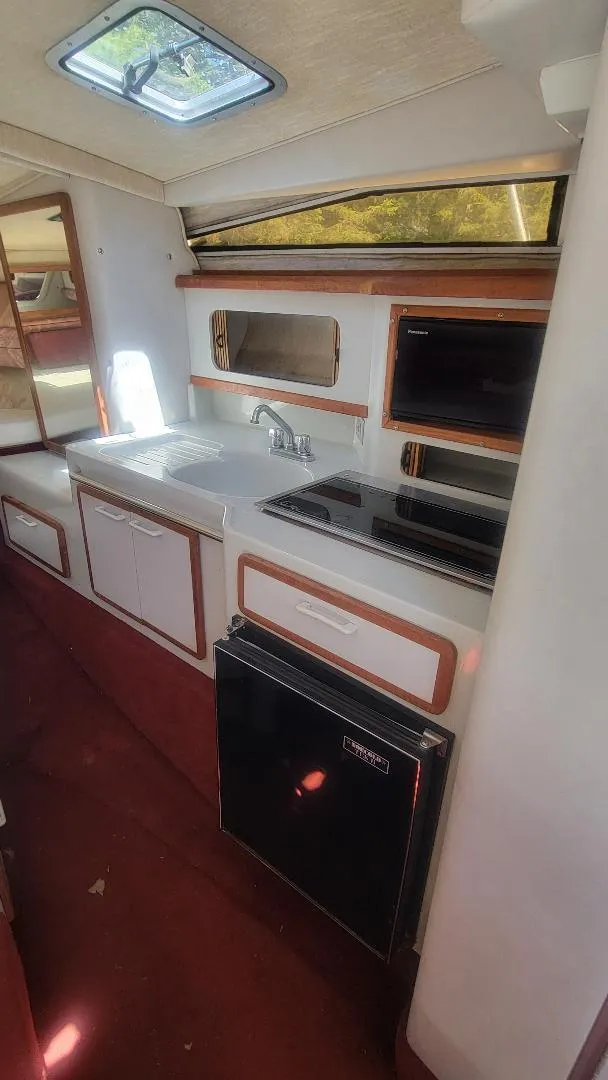 Slide: The Image of 1990 Sea Ray 270 Sundancer interior kitchen with sink, stove, and compact refrigerator. - 6