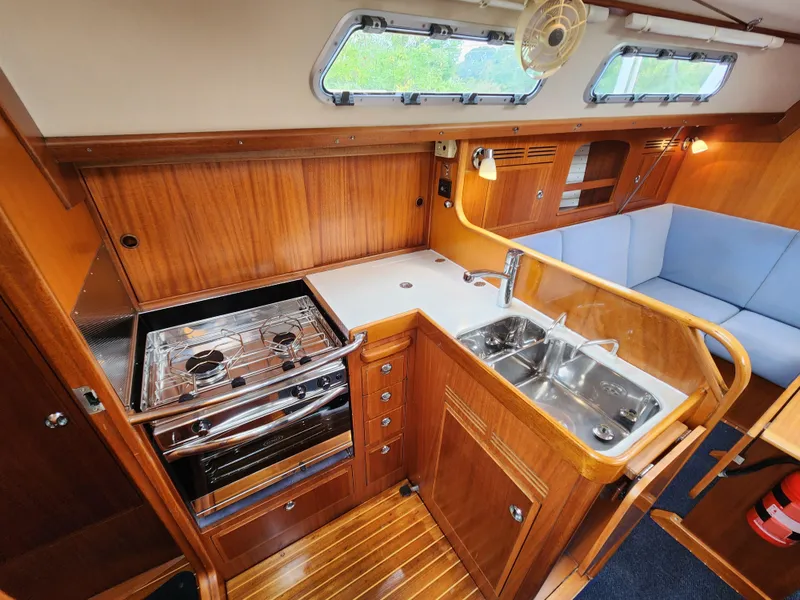 Slide: The Image of 2016 Hallberg-Rassy 342 yacht interior with wooden cabinetry, stove, sink, and seating area. - 34