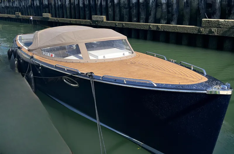 Slide: The Image of 2022 AdmiralsTender C28 boat with wooden deck, docked in calm water. - 2