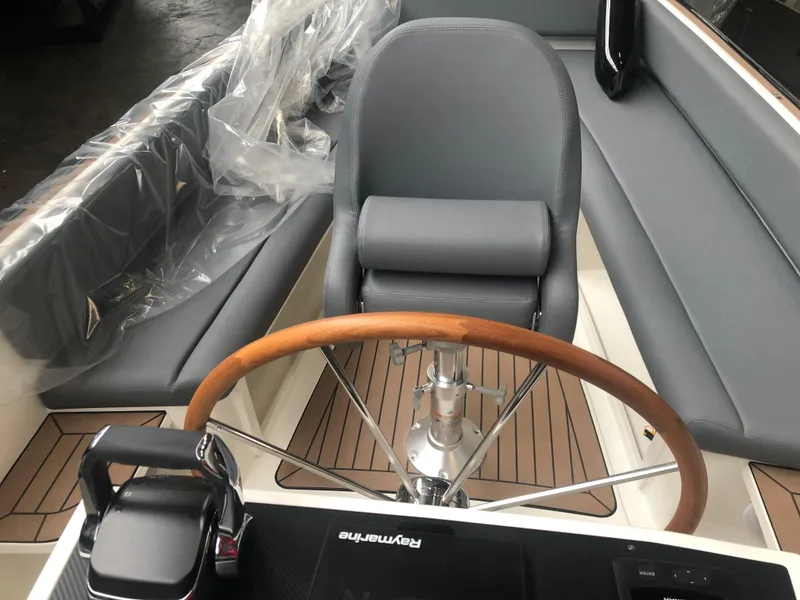 Slide: The Image of 2022 AdmiralsTender C28 boat interior with wooden steering wheel and gray seating. - 7