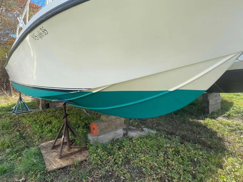 Slide: The Image of 1986 Mako 231 CC boat on stands, white and teal hull, grassy background. - 11