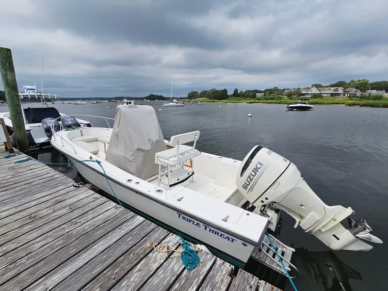 Slide: The Image of 1986 Mako 231 CC boat docked with Suzuki outboard motor, cloudy sky background. - 2