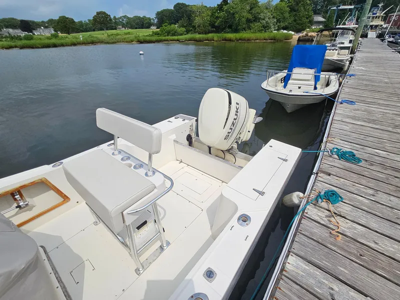 Slide: The Image of 1986 Mako 231 CC boat docked by a wooden pier on a calm river. - 6