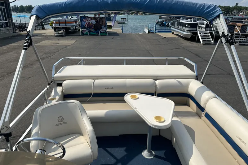 Slide: The Image of 1998 Crest II pontoon boat with beige seating and a small table, docked by the water. - 7