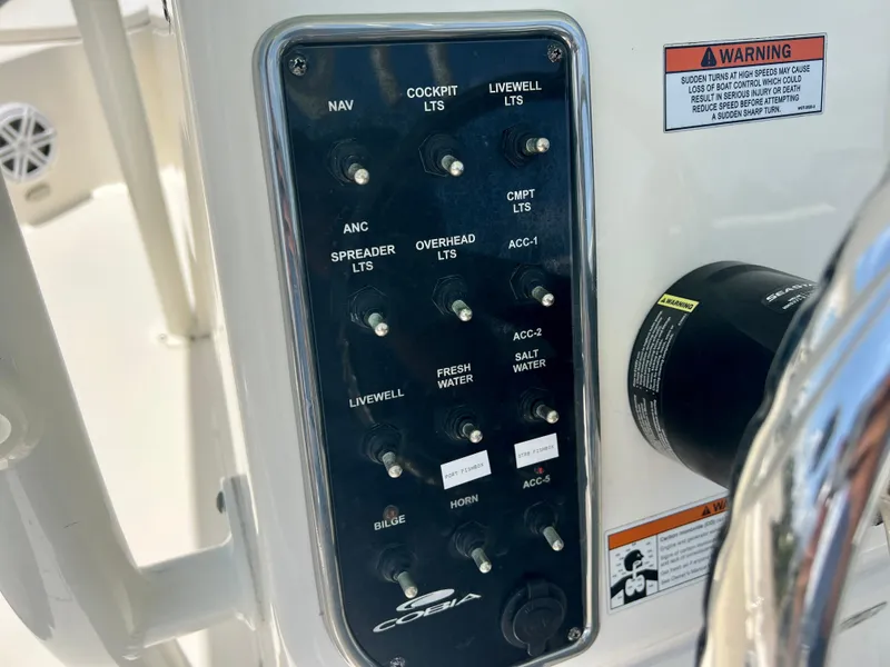 Slide: The Image of Control panel of 2023 Cobia 237 CC boat with various switches and warning labels. - 22