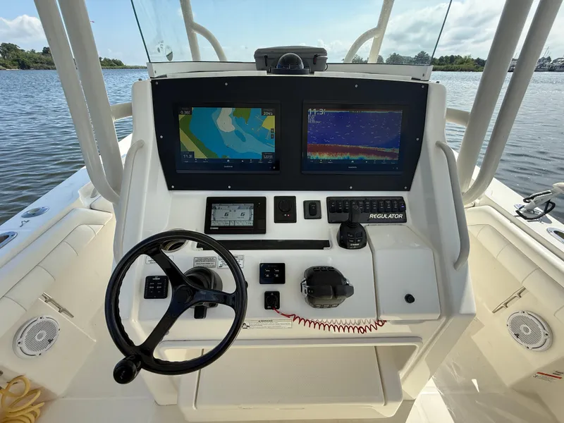 Slide: The Image of 2018 Regulator 31 boat dashboard with dual screens and steering wheel on calm water. - 23